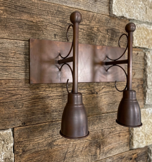 Rustic wall sconce with two metal lampshades on a wooden wall.