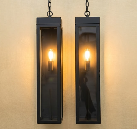 Two black outdoor pendant lights with glass panels on a beige wall.