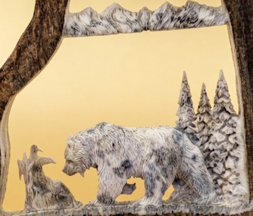 Carved Moose antler panel with a bear design against a mountainous background