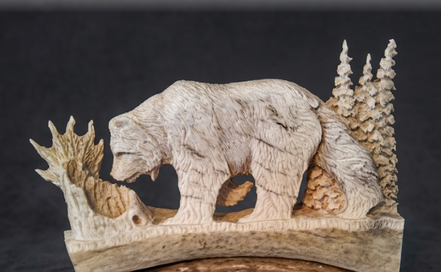 Antler carving of a bear and trees on a dark background