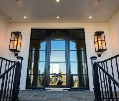 Front entrance of a house with large glass doors and decorative entryway lights.