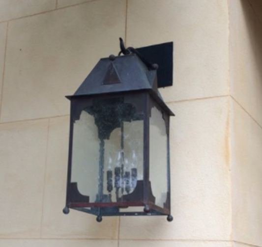 A wall-mounted copper lantern with a medieval design, featuring a solid copper top and a clear glass front casting a warm light.