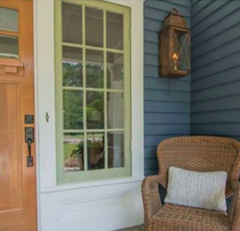 Wicker chair on a porch with a wooden door and entryway lantern.