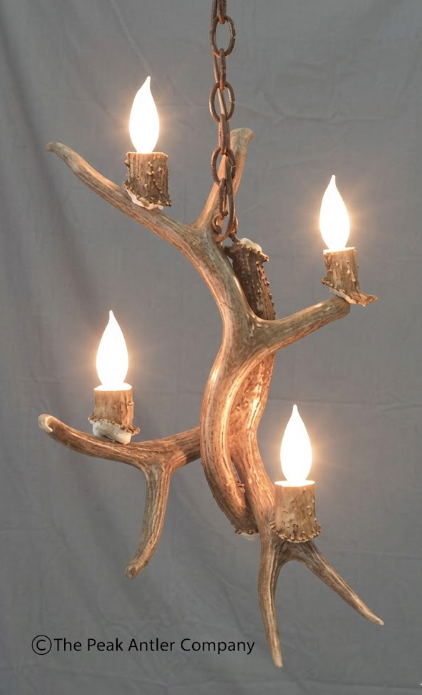 Antler chandelier with four candles on a gray background, branded 'The Peak Antler Company'.