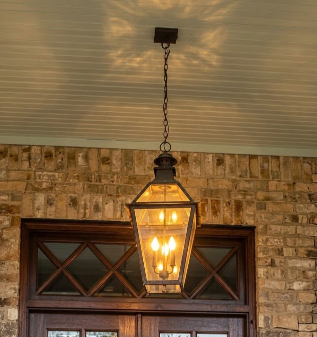 Decorative outdoor entryway foyer pendant light fixture hanging above a wooden door with stone wall background