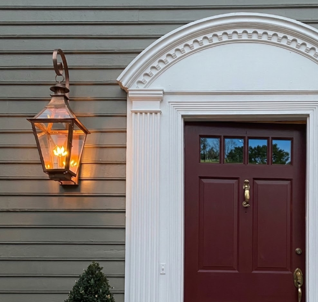 Maroon door with gold handle and entryway foyer light fixture on a gray house next to a door