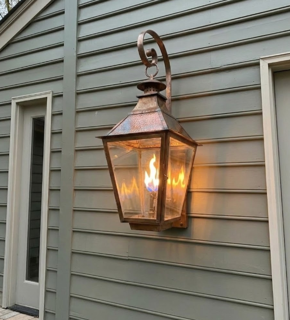 Decorative outdoor foyer entryway wall light fixture on a grey house exterior.