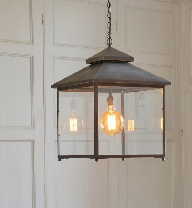 Hanging kitchen island pendant light or lantern-style light fixture with glass cover against a white paneled wall.