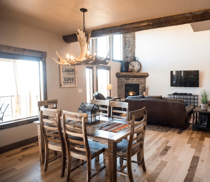 Dining area with faux moose antler chandelier and a wooden table and chairs in a living room setting.