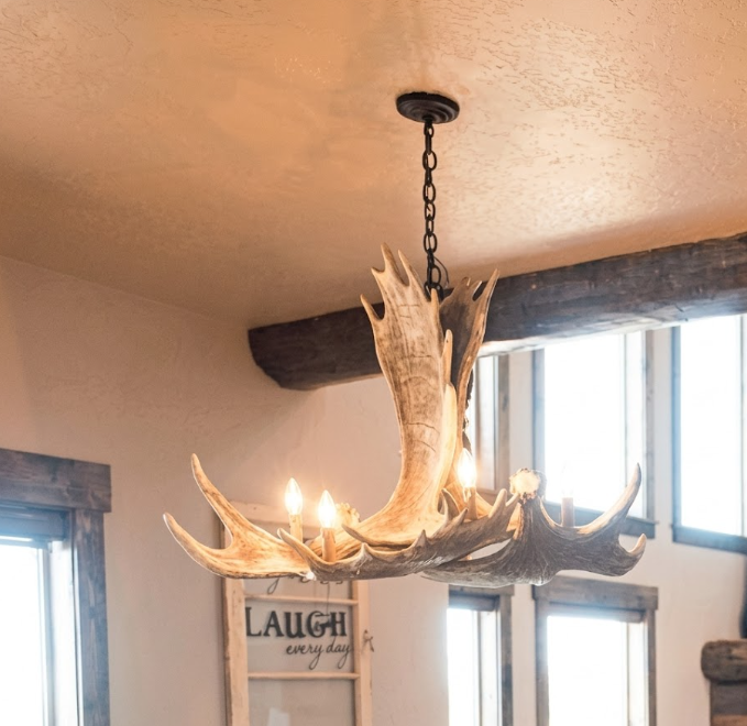 faux moose Antler chandelier hanging in a room with windows and a framed picture on the wall.