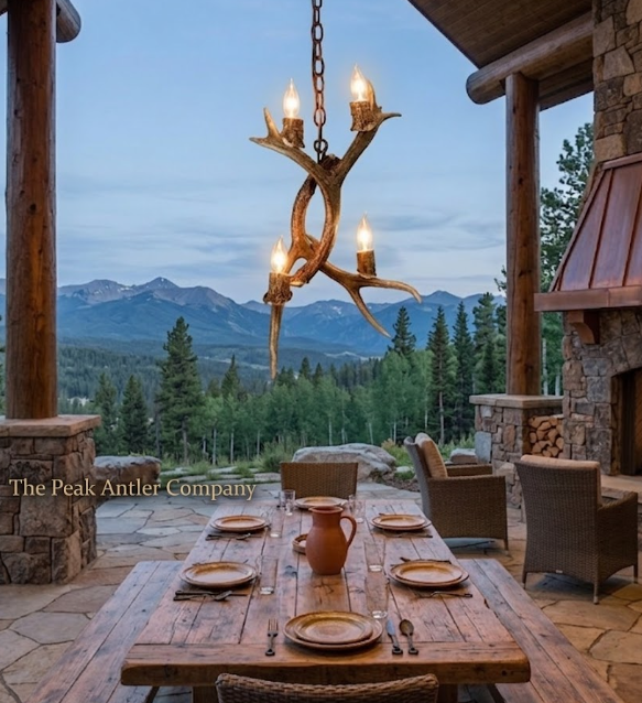Outdoor dining setting with a rustic chandelier made from antlers, surrounded by nature.