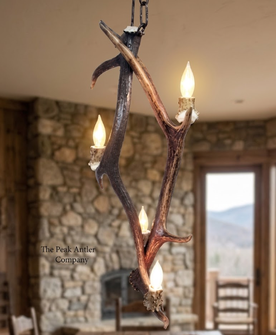 Antler chandelier with four lights in a room with stone walls and a mountain view.