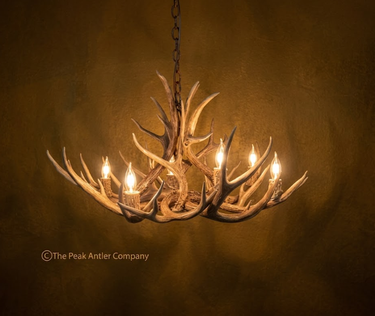 Antler chandelier with warm lighting on a dark background, featuring 'The Peak Antler Company' branding.