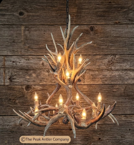 DEER Antler chandelier with warm lighting against a wooden background, featuring 'The Peak Antler Company' branding.