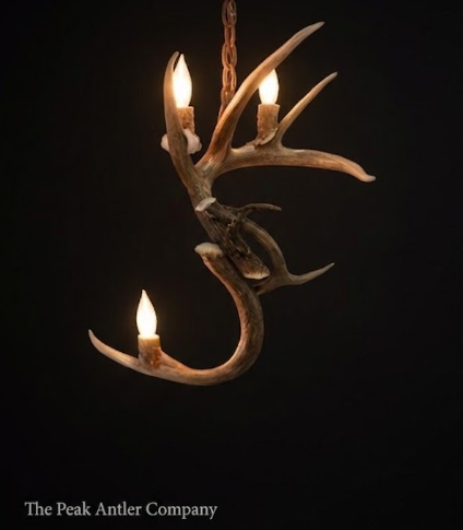 Antler chandelier with three lights on a black background, branded 'The Peak Antler Company'.