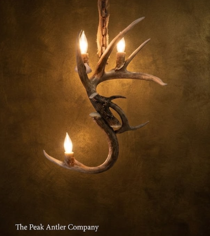 Antler chandelier with three lights on a textured brown background, featuring 'The Peak Antler Company' branding.