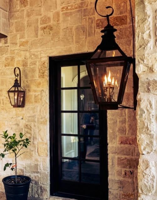 Decorative outdoor entryway lights gas lanterns on a stone wall with a black glass door.