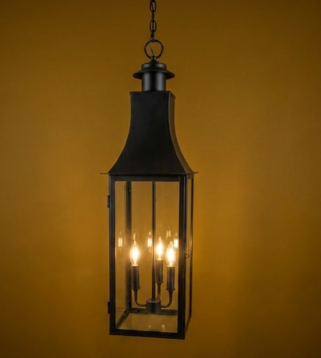 Black hanging kitchen island pendant lantern with three illuminated lights against a yellow background