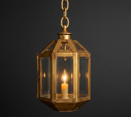 Gold pendant light lantern with a lit candle inside on a dark background