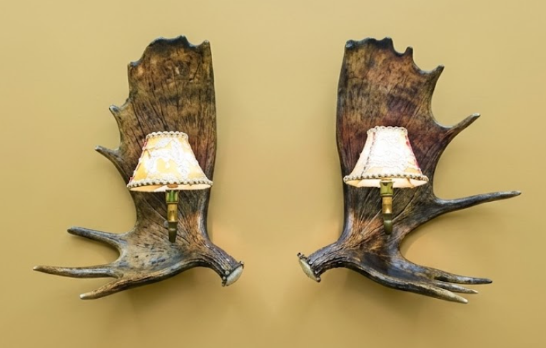 Two wall sconces made from antlers with lampshades on a beige background