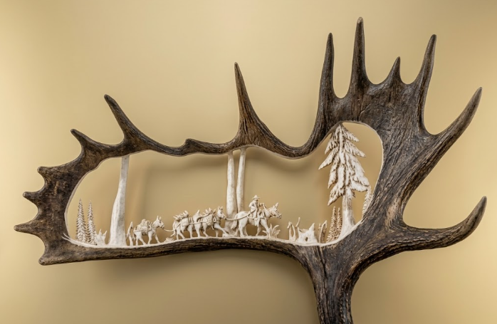 Decorative wall art with packstring moose antler carving featuring a silhouette of a forest and animals on a beige background.