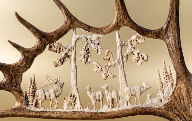 Decorative wall art with moose antler carving deer and trees on a wooden antler frame.