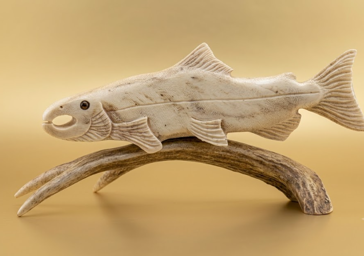Carved fish figurine on a branch against a beige background