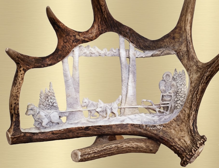 Decorative antler frame with a winter scene of people and animals in a snowy landscape.