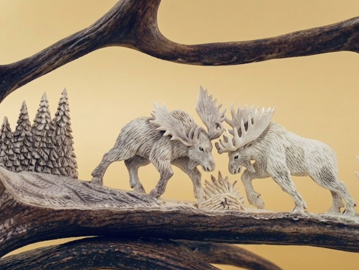 Carved scene of two moose fighting on a wooden base with a beige background