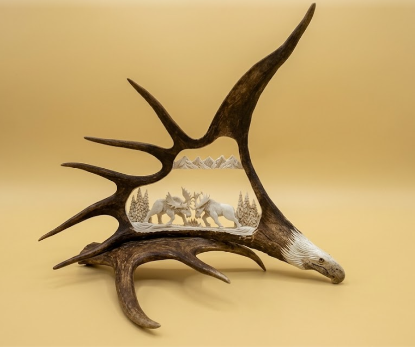 Decorative  antler with a carved scene of two moose and trees on a beige background
