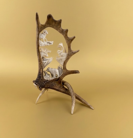 Decorative moose antler with embedded figurines on a gold background