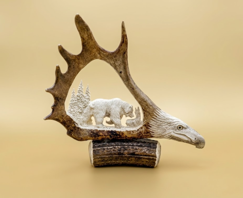 Decorative piece with antlers and a carved bear scene on a beige background
