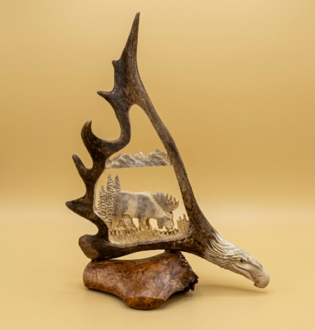 Caribou real antler shed with eagles head rafted into the base and a browsing moose in the mountain scene, with a tan background.
