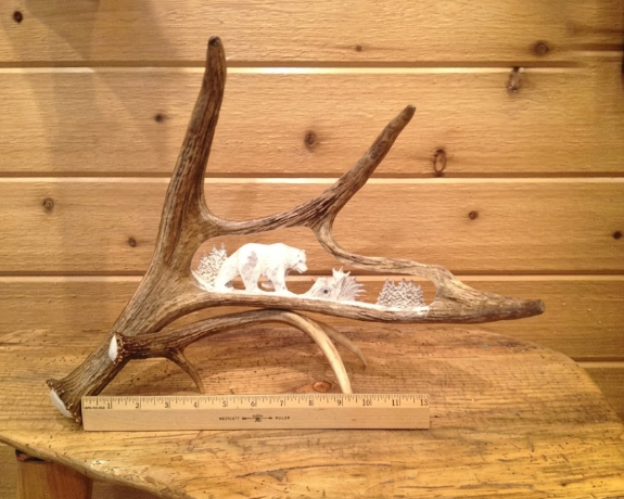 Decorative antler with bear in the forest carvings accompanied by a ruler for scale.