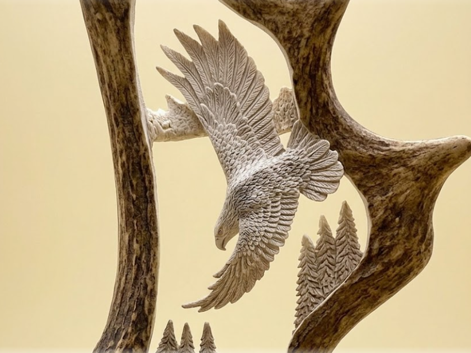 Carved moose antler sculpture of an eagle flying among  the trees, with a beige background
