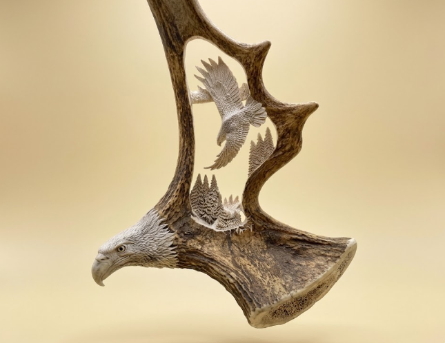 Decorative moose antler with eagle carvings on a beige background