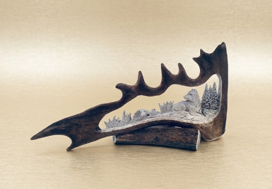 Decorative desk carving of a mid day napping wolf on a caribou antler featuring a snowy landscape with trees.