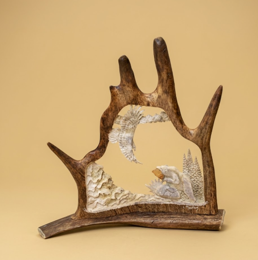 Hand crafted antler carving, desk mount, on a tan background of a soaring eagle and a fishing bear.