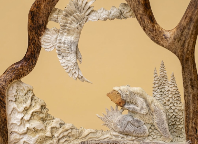 Carved moose antler scene with a fishing bear and soaring eagle on a beige background