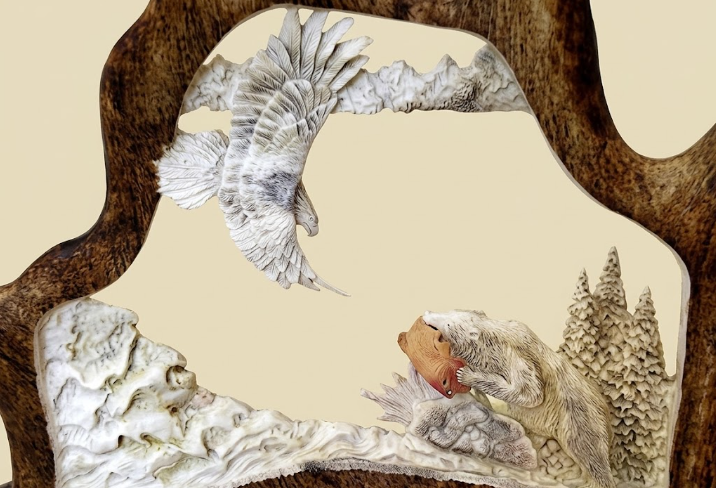 Moose antler frame with carvings of an eagle and a bear on a beige background
