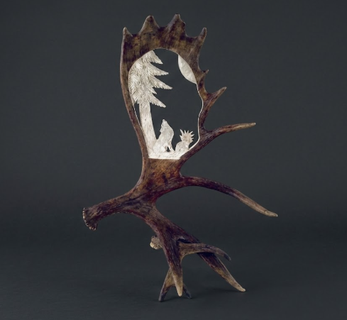 Decorative piece with moose antler design featuring cut-out wolf howling at moon on a dark background