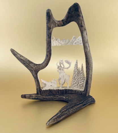 Decorative antler with a carved scene of a caribou and trees on a beige background