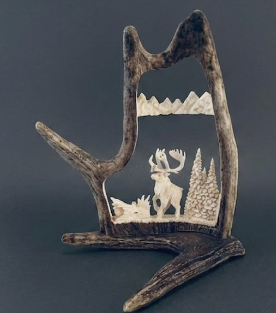 Alaskan caribou antler carving from a caribou antler depicted in a mountain scene.