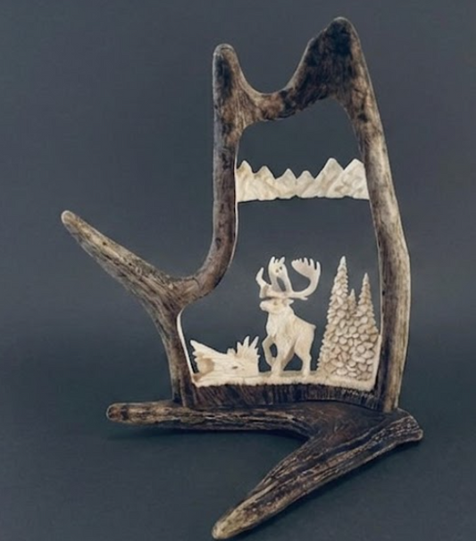 Alaskan caribou antler carving from a caribou antler depicted in a mountain scene.
