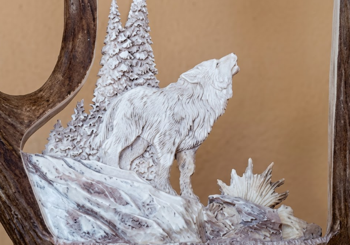 Moose antler sculpture of a wolf howling at the moon with trees in the background