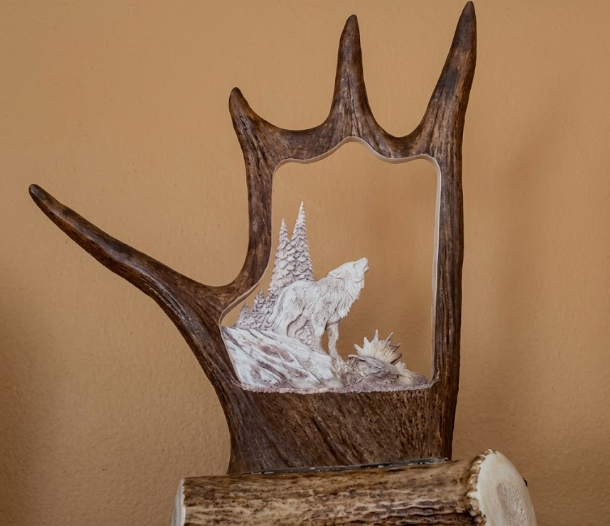 Moose antler  carving with a cutout design of a wolf and landscape on a beige background