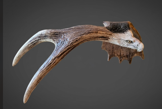 Decorative antler with an eagle head design on a dark background