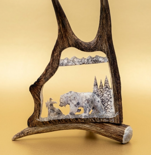 Moose Antler  frame with a carved scene of a bear in a snowy landscape on a beige background