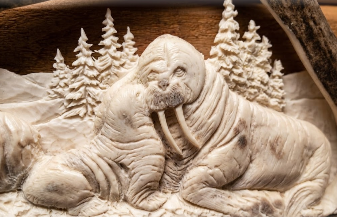 Carved walrus in a natural setting with trees on an antler background