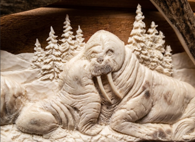 Carved antler  of a walrus momma and baby with a forest background